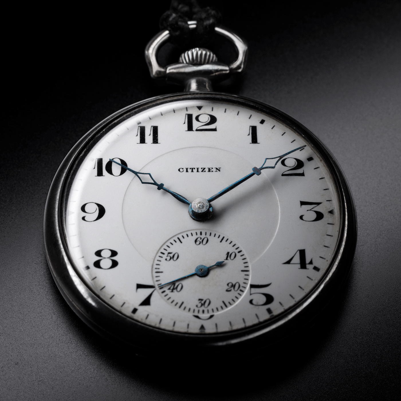 Gros plan d'une montre de poche Citizen, montrant l'heure et les détails sur fond noir.