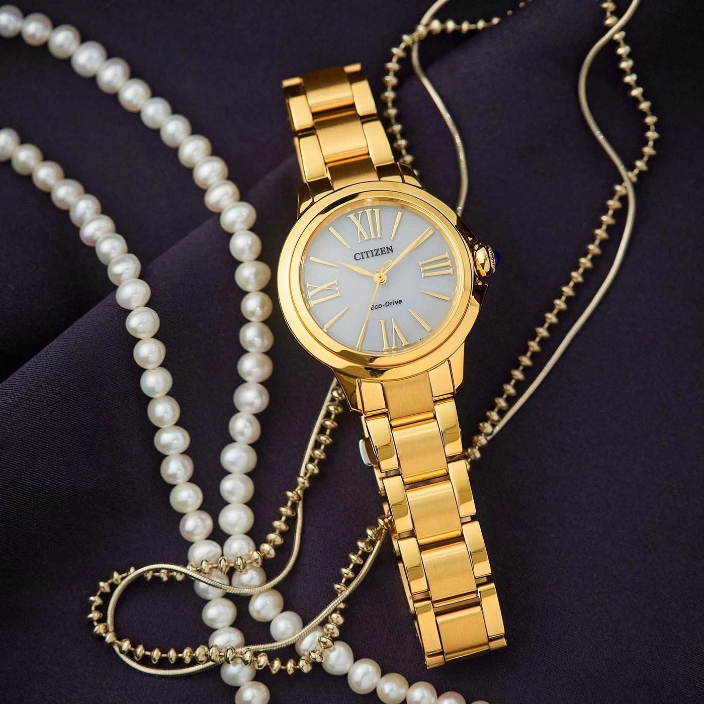 Montre Citizen dorée avec collier de perles sur tissu sombre.