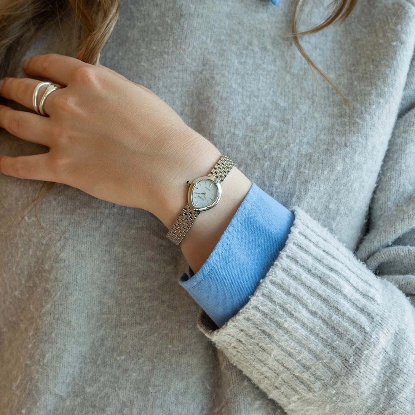 Eine Frau trägt eine silberne Uhr und einen goldenen Ring an ihrem Handgelenk.
