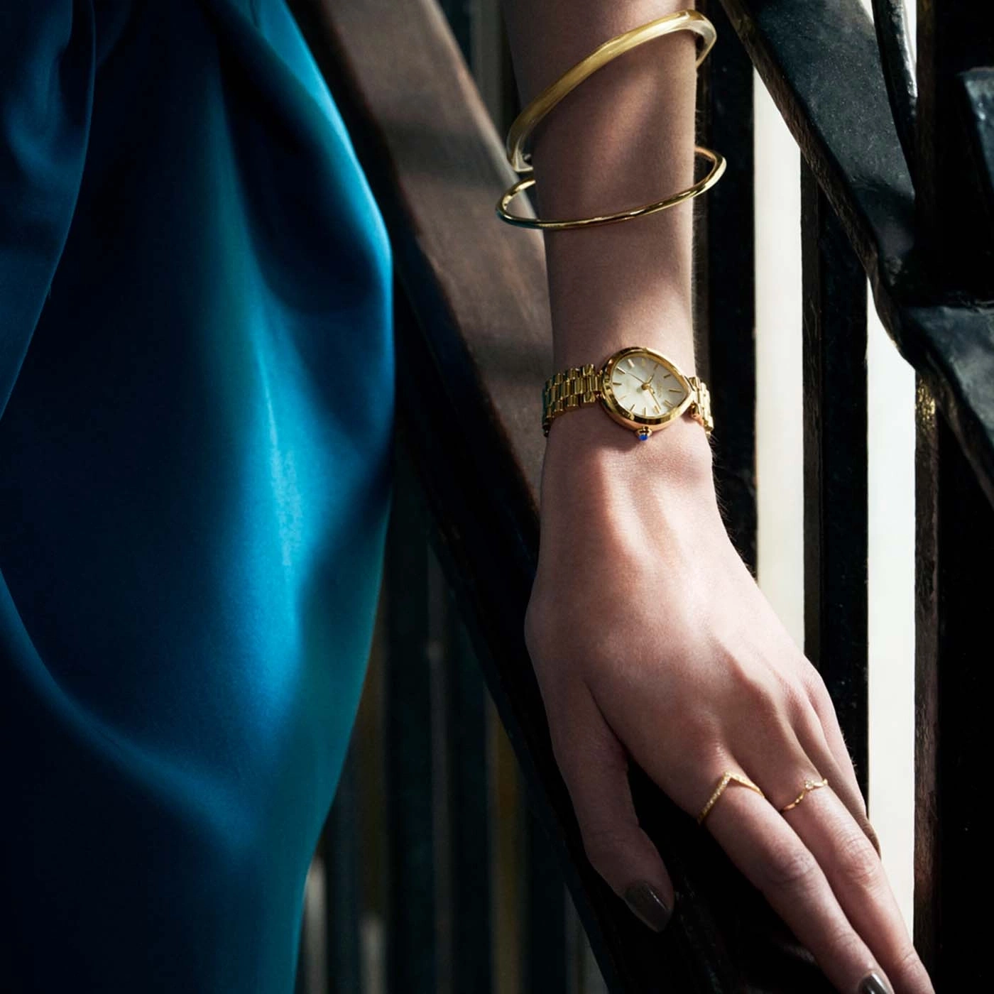Eine Frau trägt ein blaues Kleid, eine goldene Uhr und Ringe.
