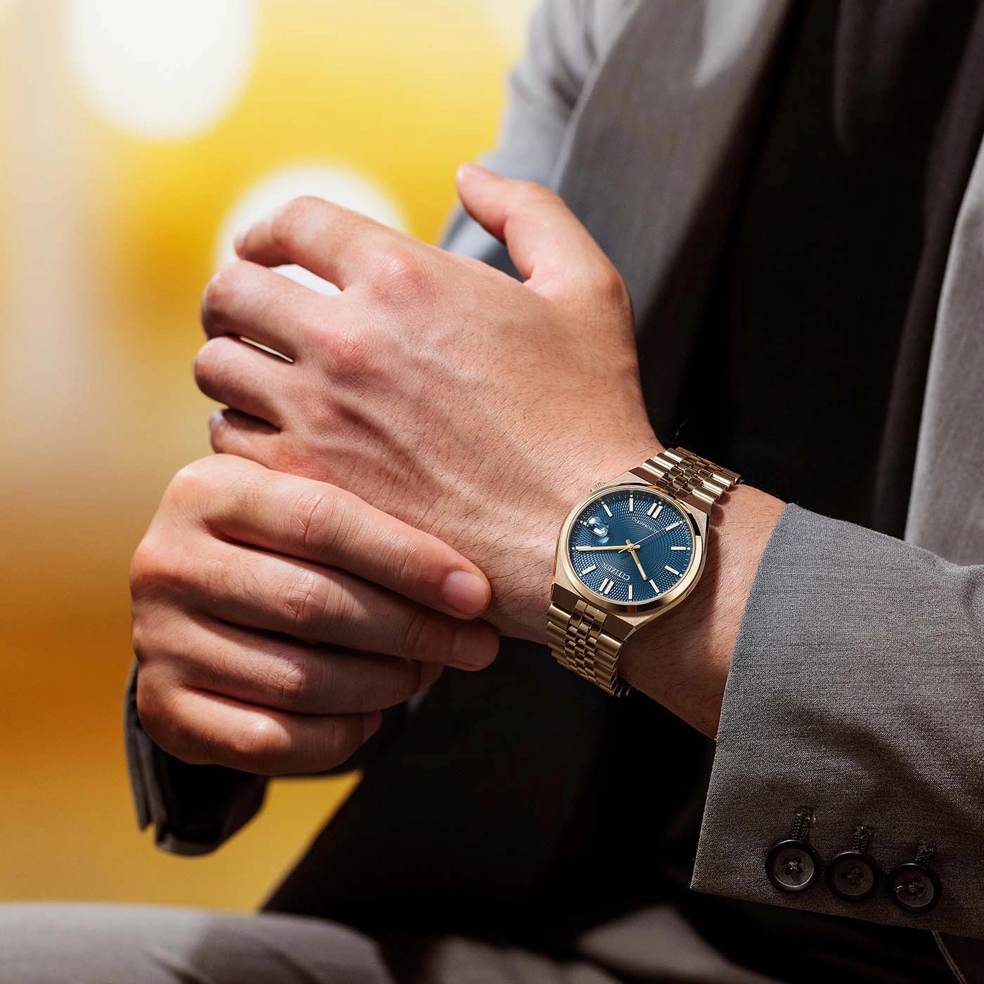 Homme en costume gris ajustant sa montre dorée au cadran bleu.