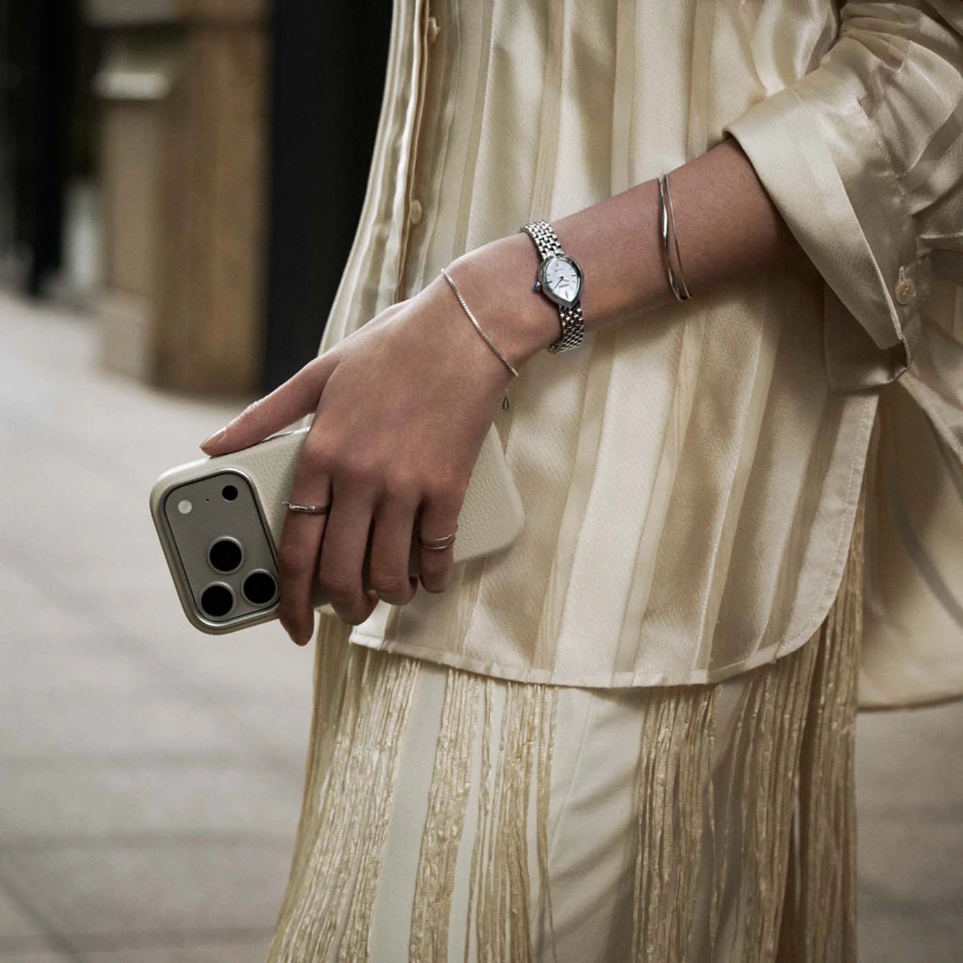 Eine Frau hält ein Handy und trägt eine Uhr und Armbänder.