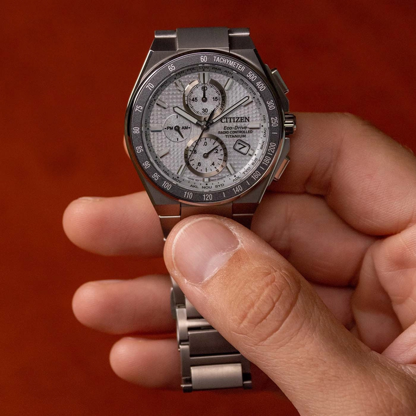 Eine Hand hält eine silberne Citizen-Uhr vor einem orangefarbenen Hintergrund.