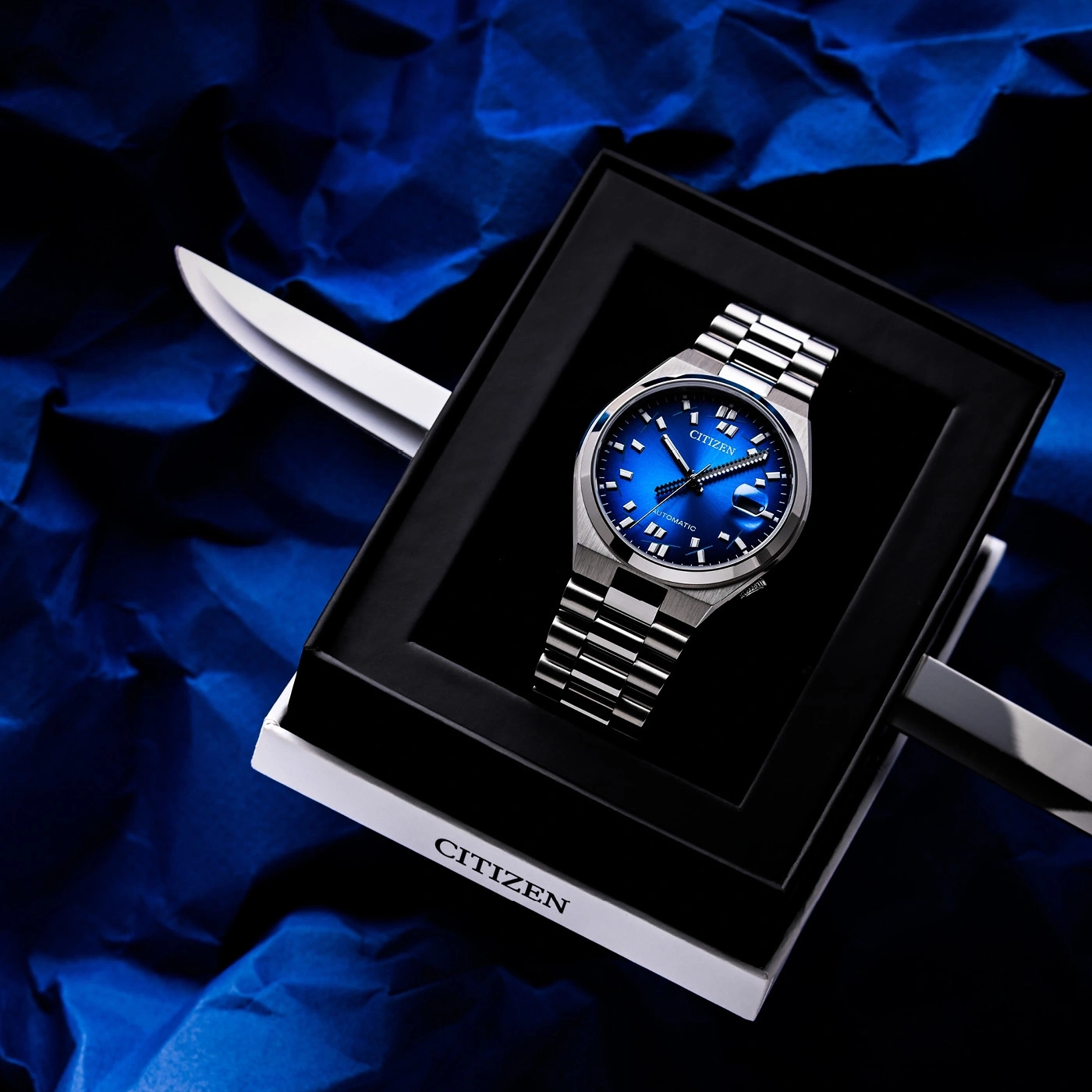 Blaue Citizen Automatik-Uhr in Box auf zerknittertem blauen Hintergrund.