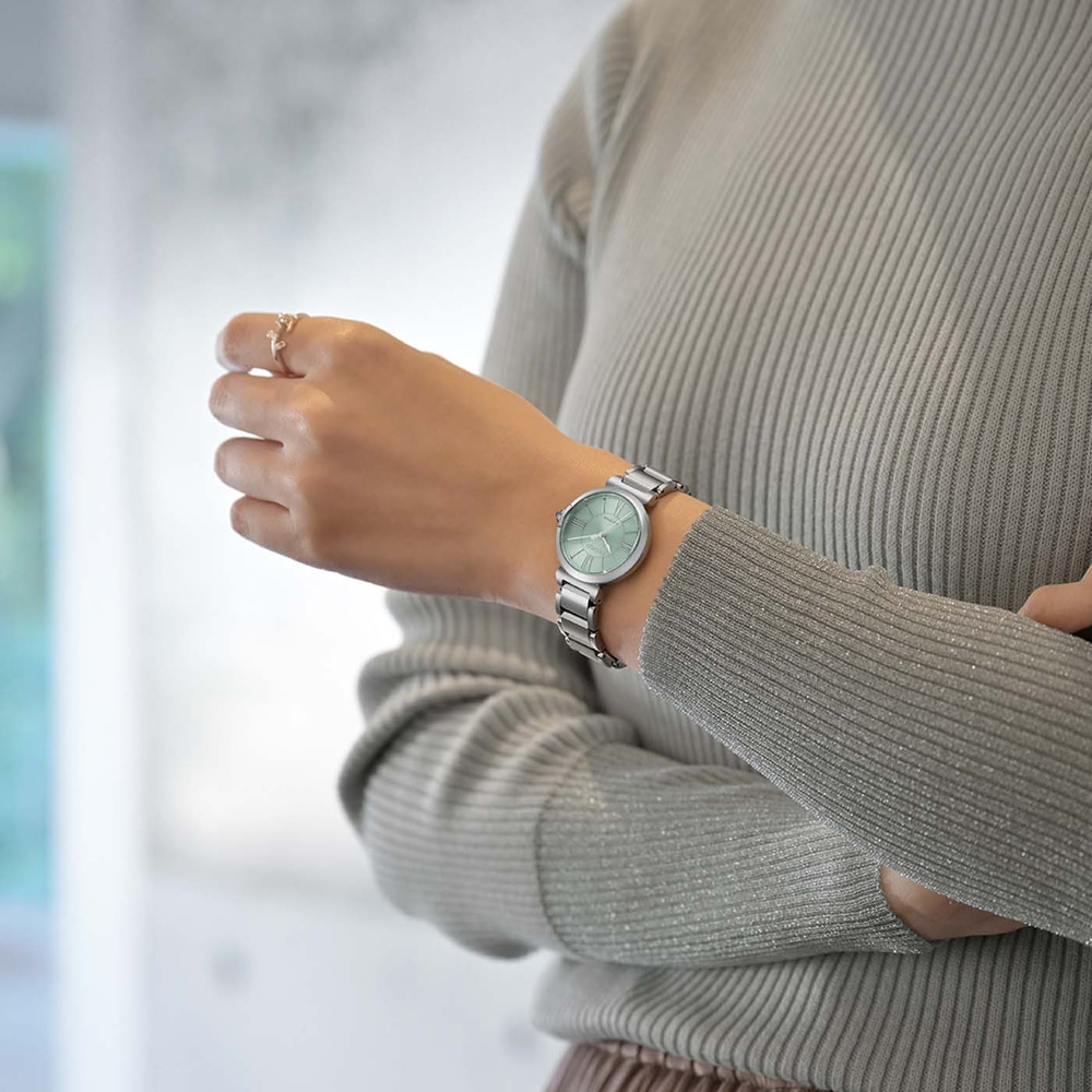 Une femme portant une montre argentée et un pull gris.