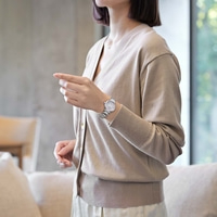 Femme portant un gilet beige et une montre argentée, pointant.