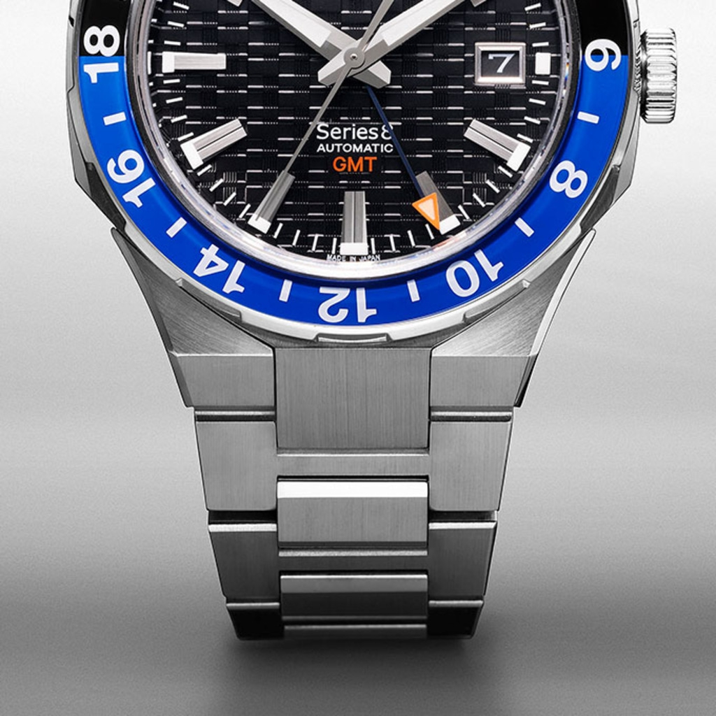 Nahaufnahme einer silbernen Uhr mit blauer Lünette und schwarzem Zifferblatt.