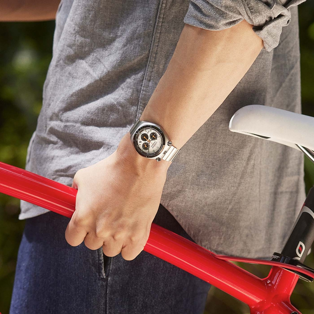 Personne en chemise grise tenant un cadre de vélo rouge, portant une montre.
