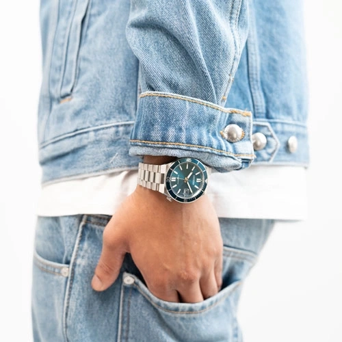 Mann trägt eine Jeansjacke mit einer blauen Uhr am Handgelenk.
