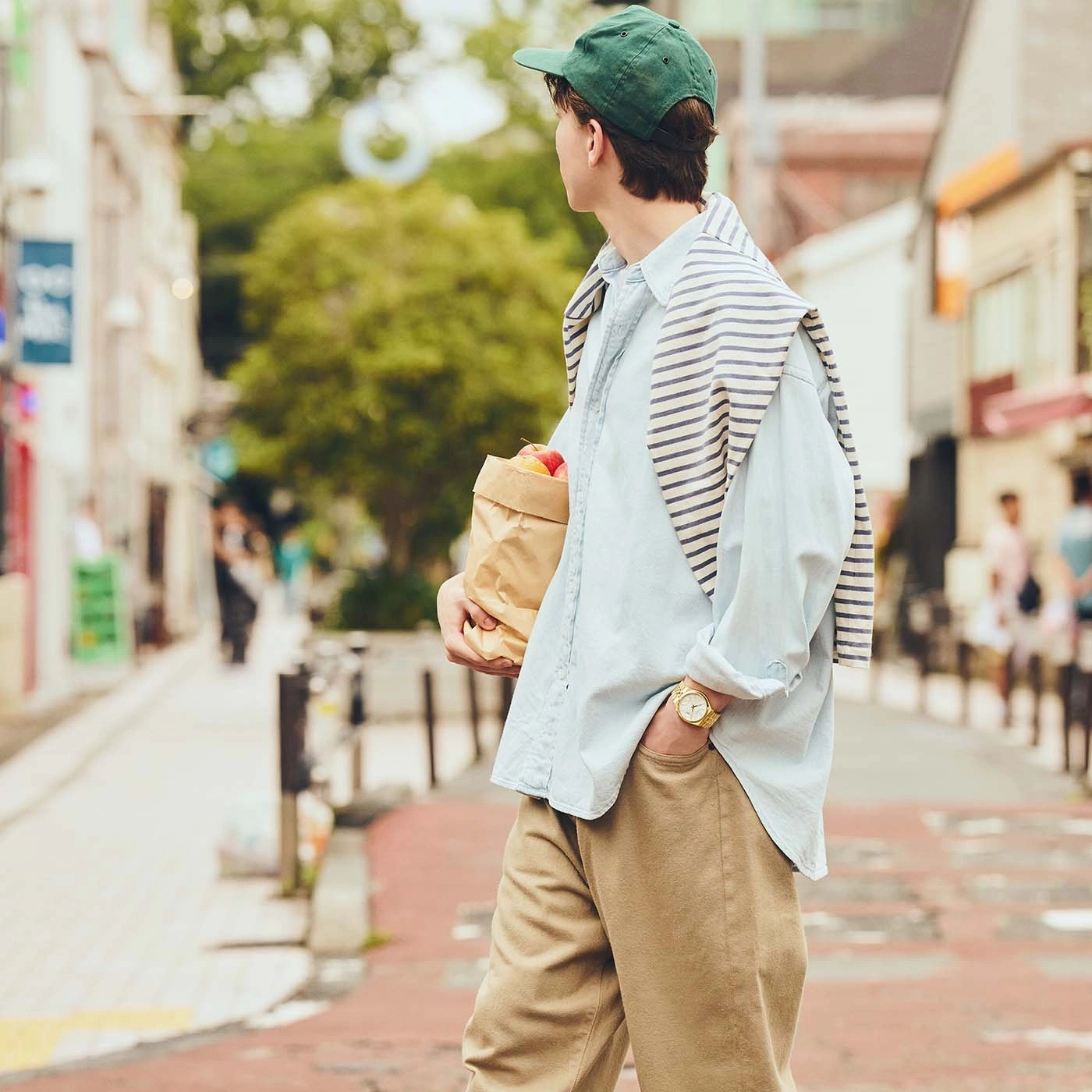Mann mit Papiertüte und Pullover über den Schultern in einer Straße.