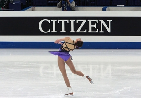 Patineuse artistique en robe violette effectuant une pirouette sur la glace.