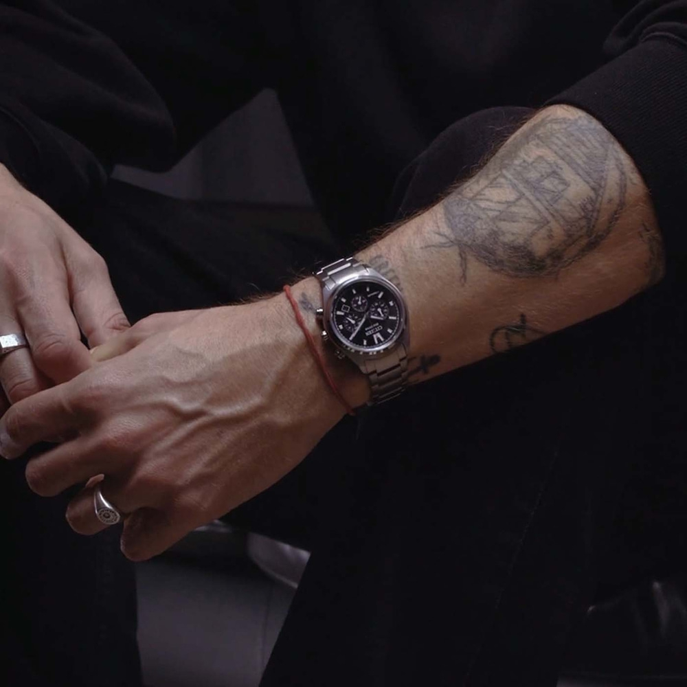 Gros plan du bras tatoué d'un homme portant une montre et des bagues.