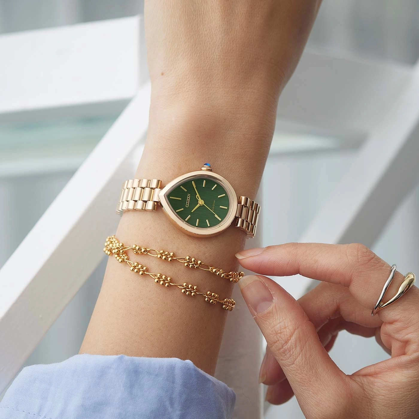 Eine Frau trägt eine grüne Eco-Drive-Uhr mit einem goldenen Armband und einem Ring.