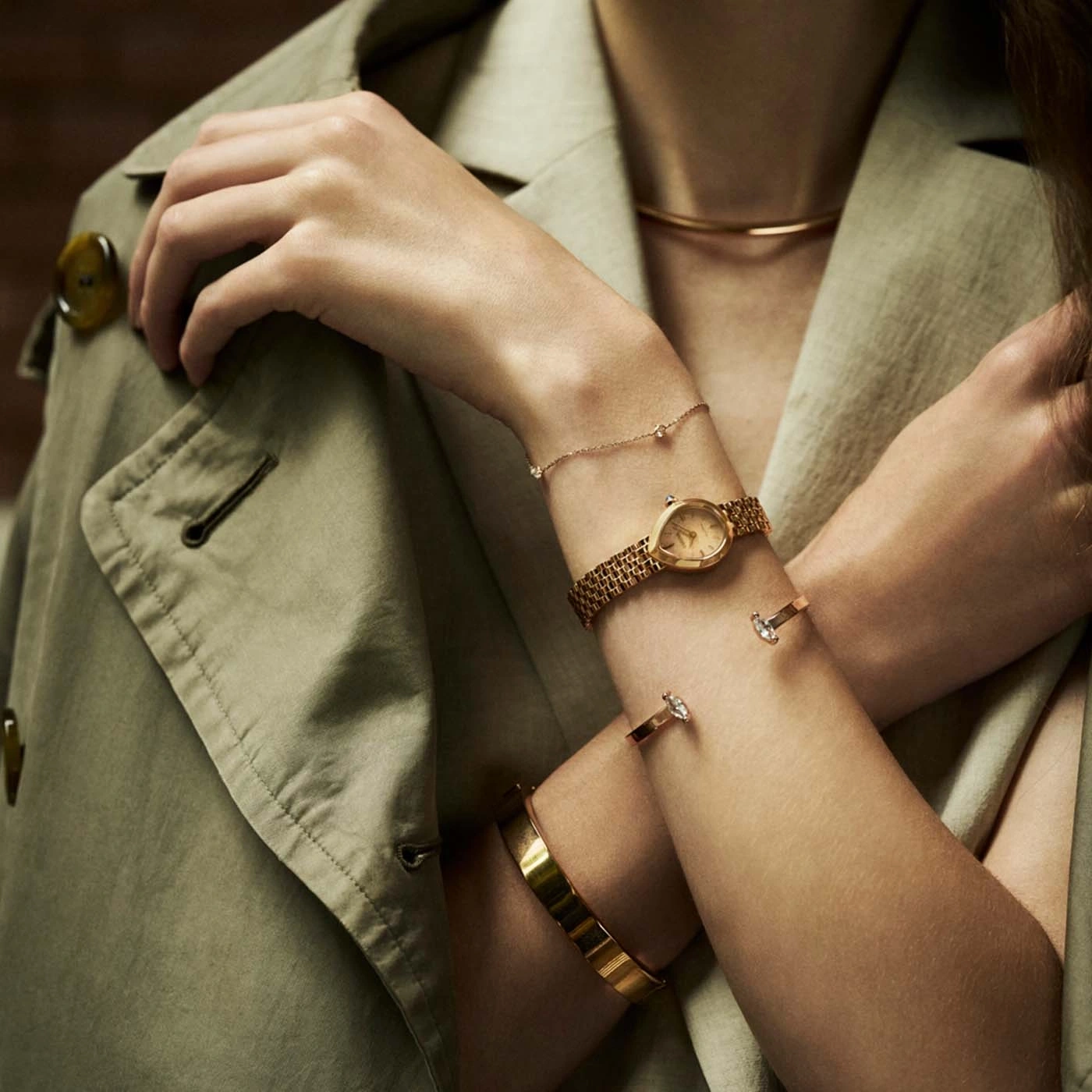 Eine Frau trägt eine Jacke und Goldschmuck, darunter eine Uhr und Armbänder.