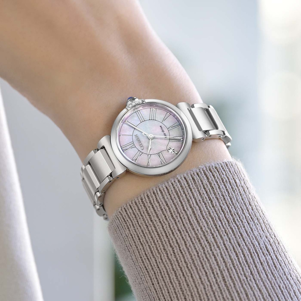Le poignet d'une femme porte une montre argentée avec un cadran en nacre.