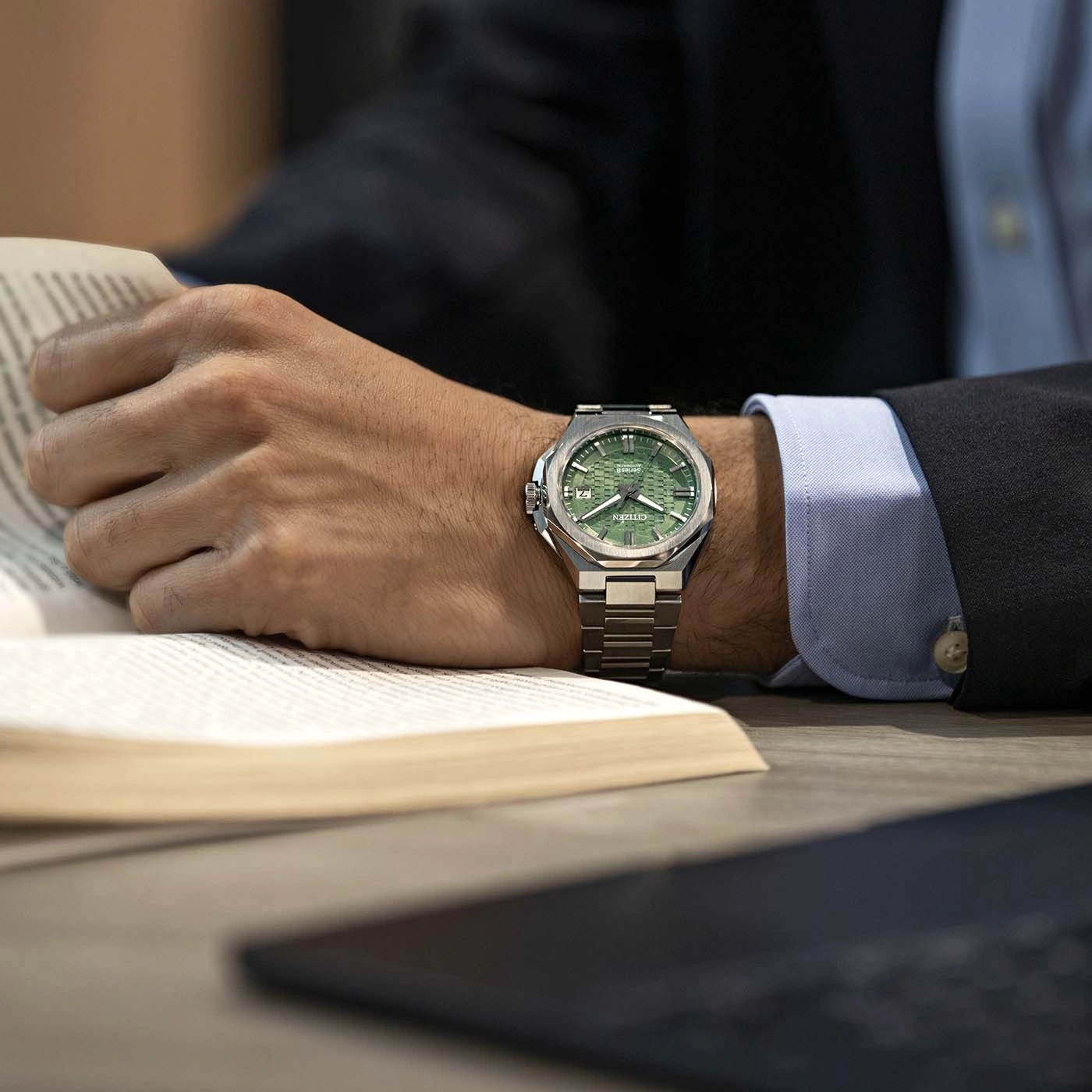 Geschäftsmann mit grüner Uhr liest ein Buch am Schreibtisch