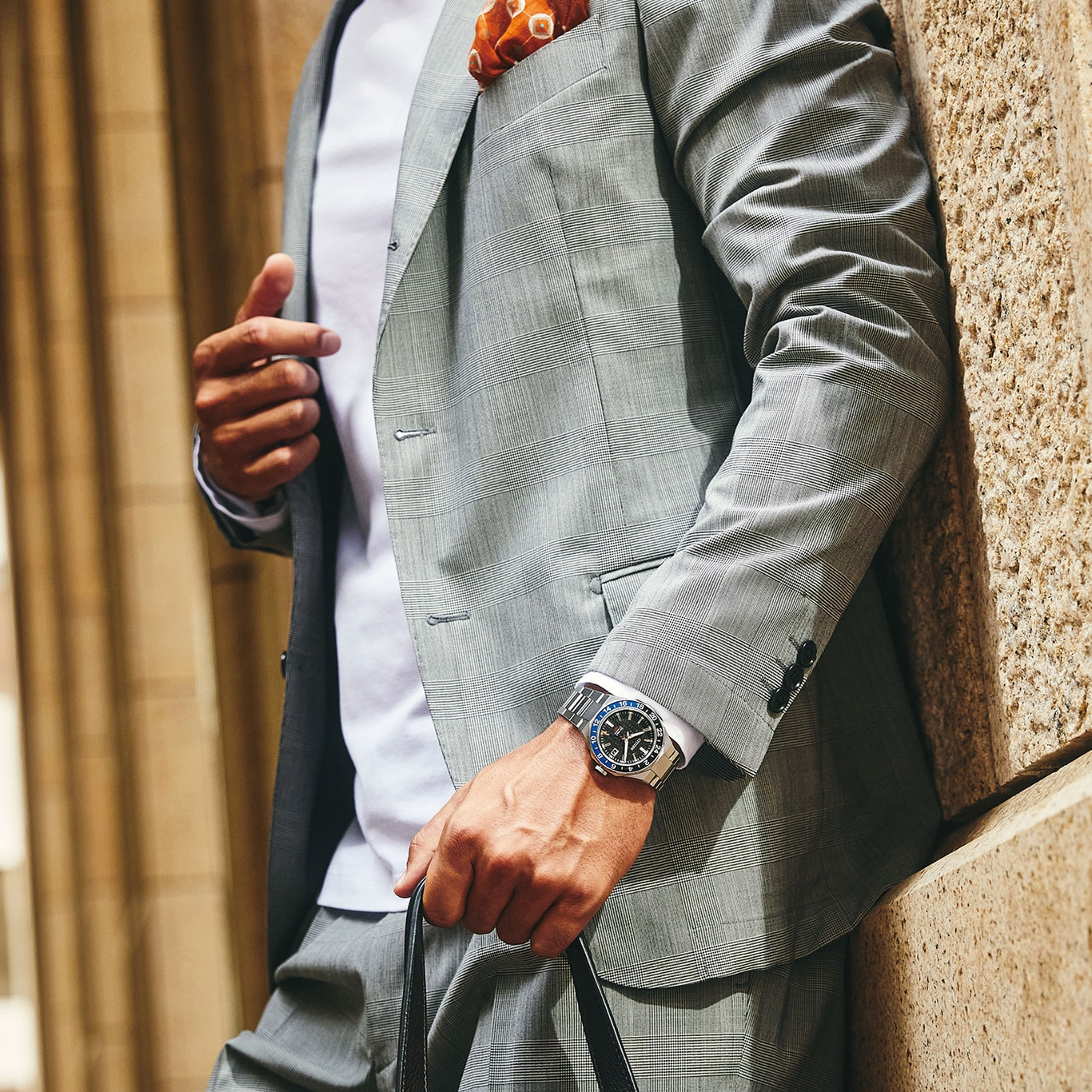 Mann im Anzug mit Uhr und Einstecktuch lehnt an einer Wand