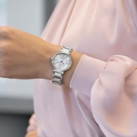 Le poignet d'une femme portant une montre argentée avec un cadran blanc et des chiffres romains.