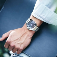 Homme portant une montre argentée, tenant un dossier bleu foncé.