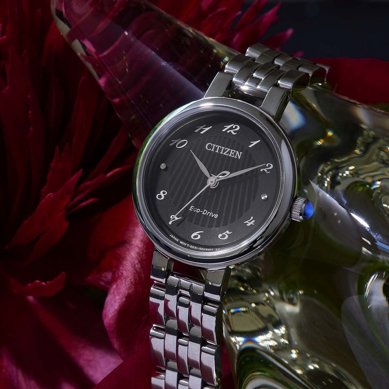 Une montre Citizen Eco-Drive argentée repose sur un fond rouge et réfléchissant.