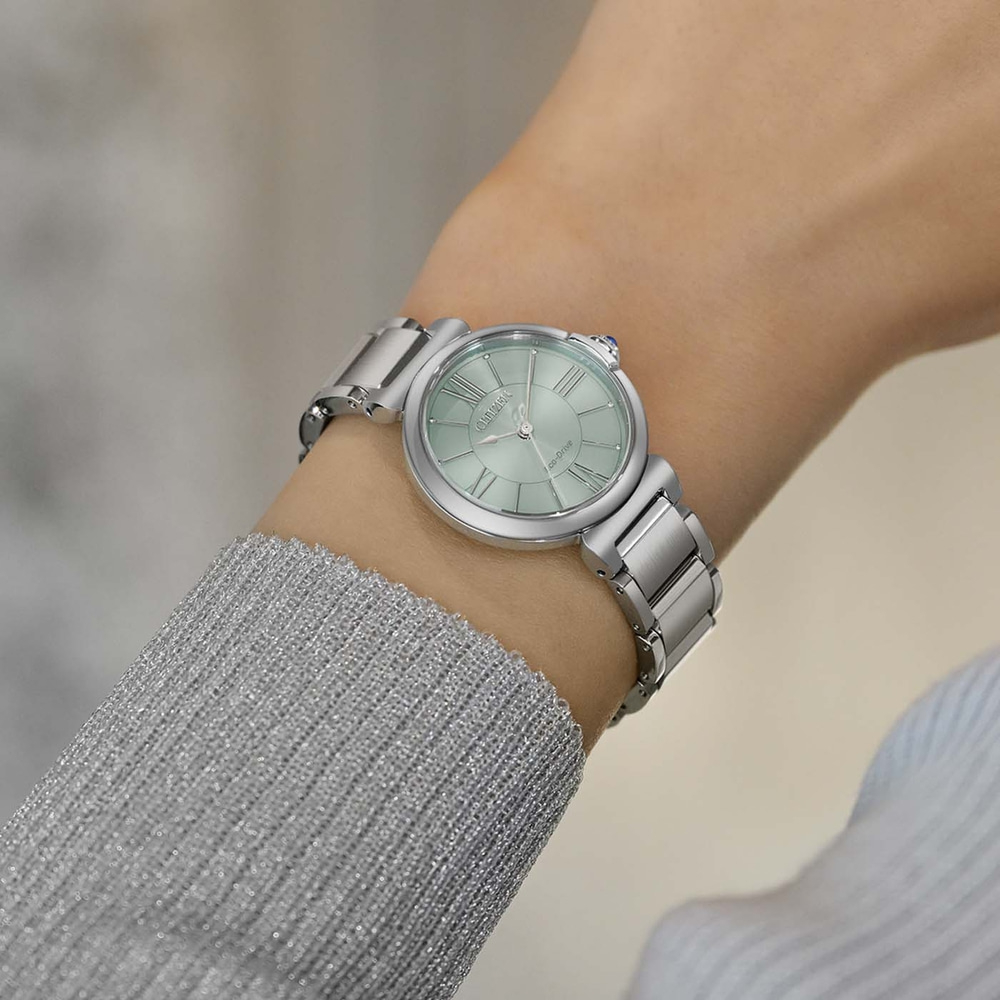 Le poignet d'une femme portant une montre argentée avec un cadran vert clair.