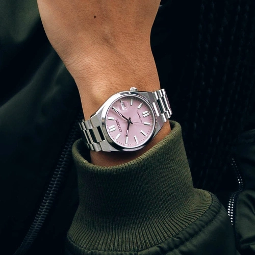 Citizen-Uhr mit rosa Zifferblatt an einem Handgelenk, grüne Jacke.