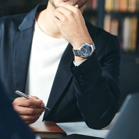 Homme en costume avec montre, tenant un stylo, réfléchissant, réunion d'affaires, bureau