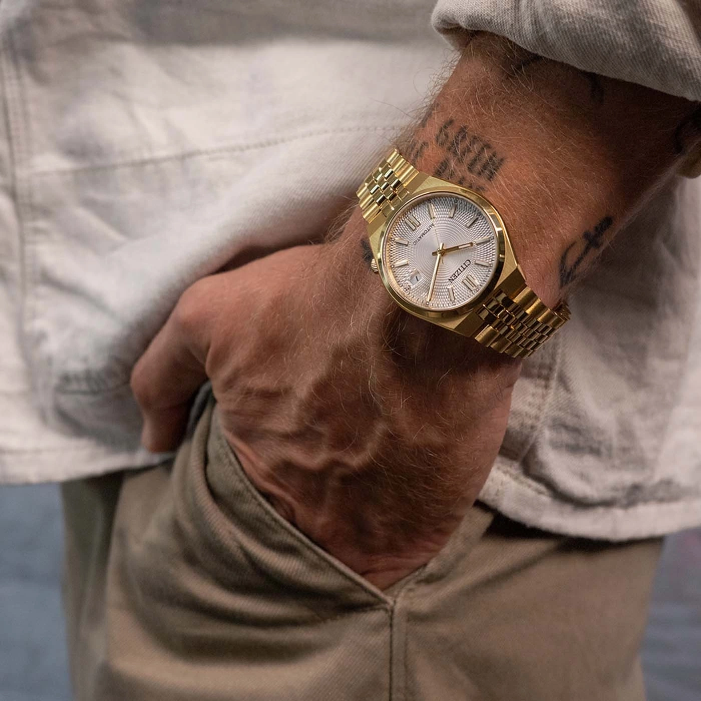 Mann mit goldener Citizen-Uhr und Metallarmband am Handgelenk.