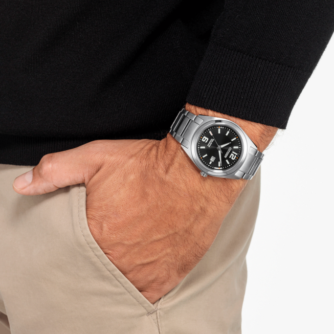 Mann mit Citizen-Uhr, schwarzem Pullover und beigefarbener Hose.
