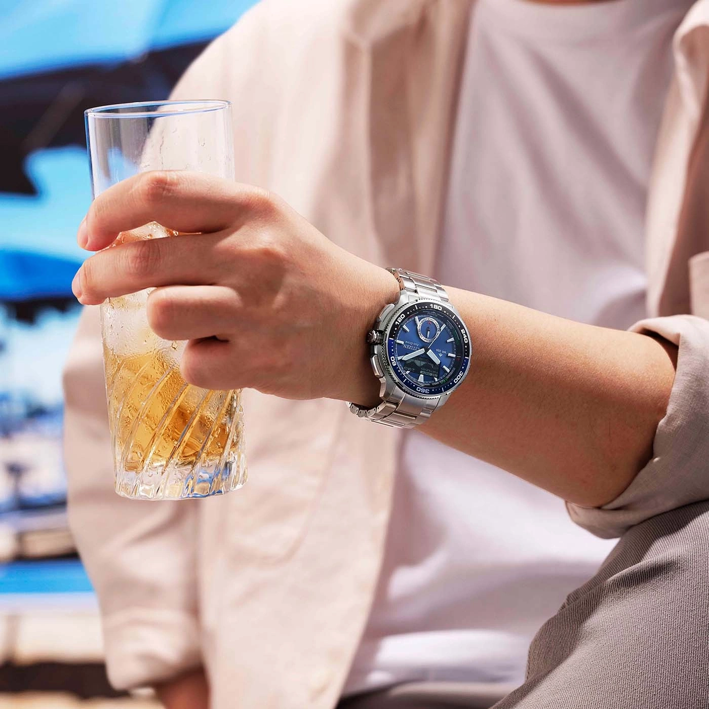 Un homme tient un verre rempli de glaçons et d'une boisson ambrée, portant une montre argentée au poignet.