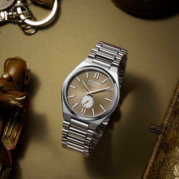 Citizen-Uhr mit silbernem Armband auf goldener Oberfläche mit Zubehör.
