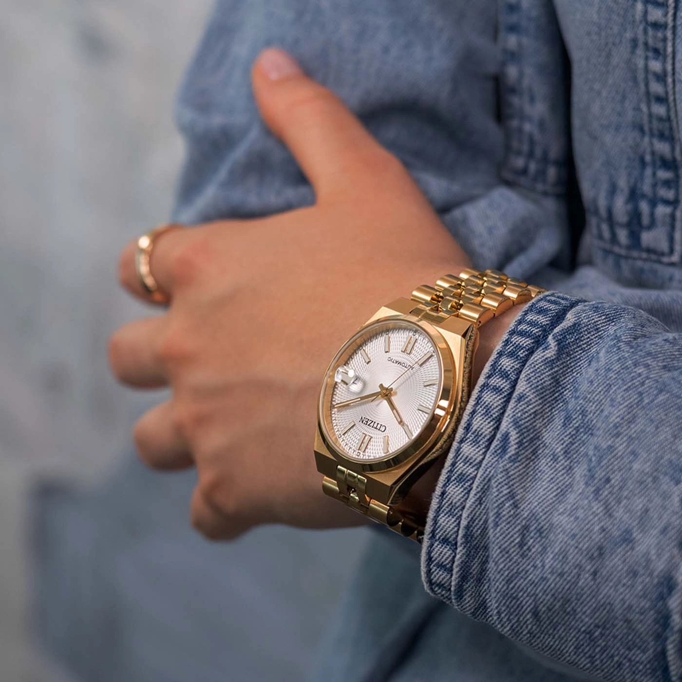 Eine Frau trägt eine goldene Citizen-Uhr an einem Jeans-Armband.