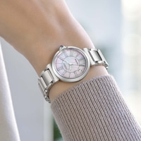 Le poignet d'une femme porte une montre argentée avec un cadran en nacre.