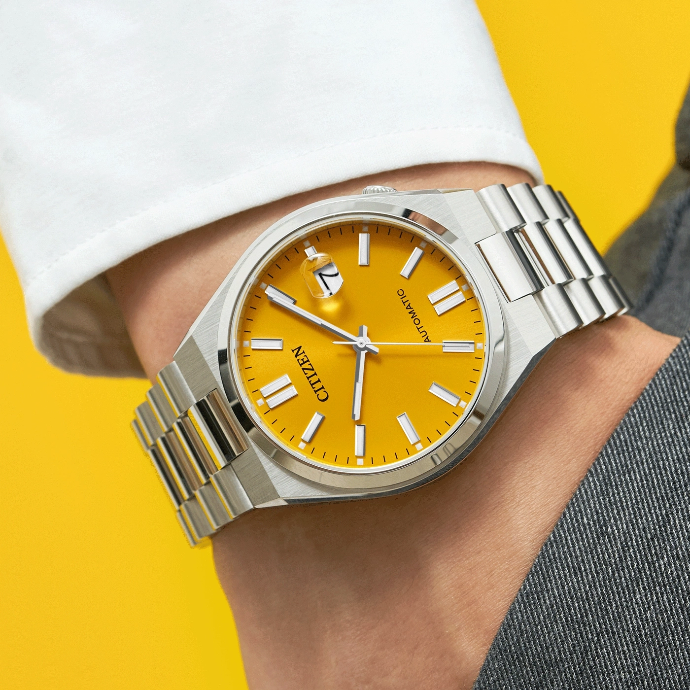 Eine Citizen Automatik-Uhr mit einem leuchtend gelben Zifferblatt an einem Handgelenk.