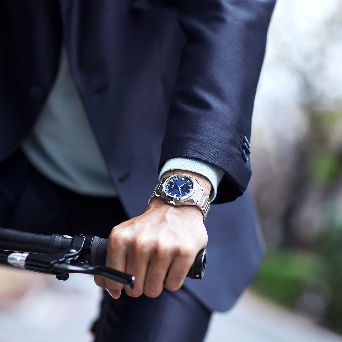 Mann mit Uhr, hält Fahrradlenker, trägt Anzug. Nahaufnahme.