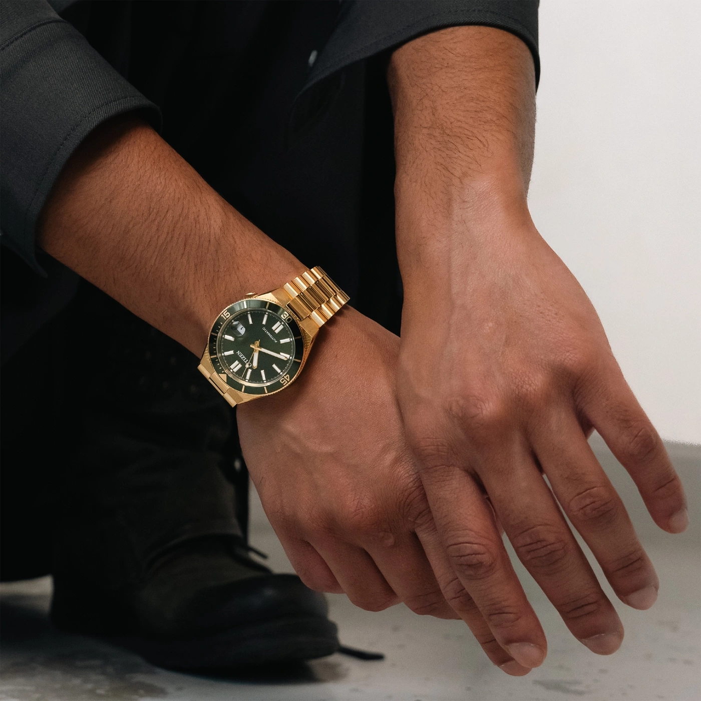 Ein Mann trägt eine goldene Uhr mit grünem Zifferblatt am Handgelenk.