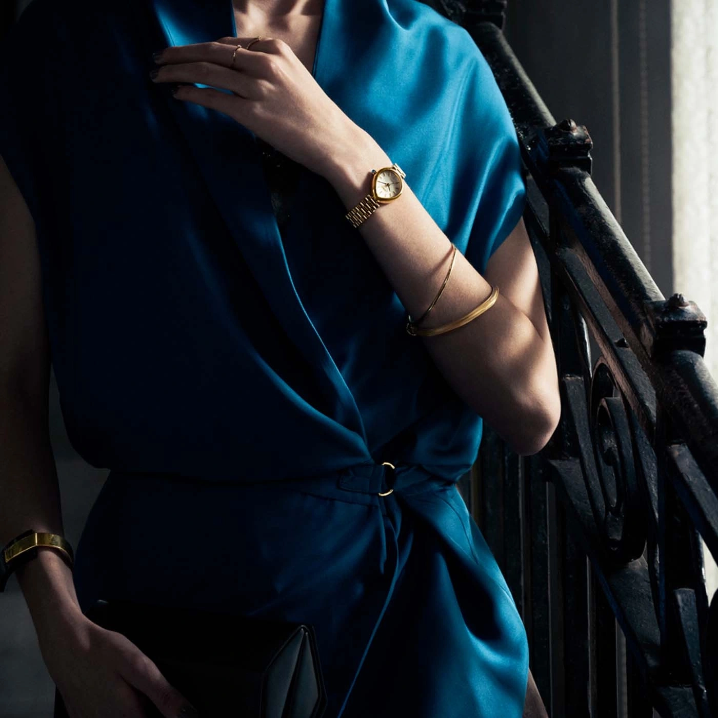 Frau in blauem Kleid mit goldener Uhr und Armband.