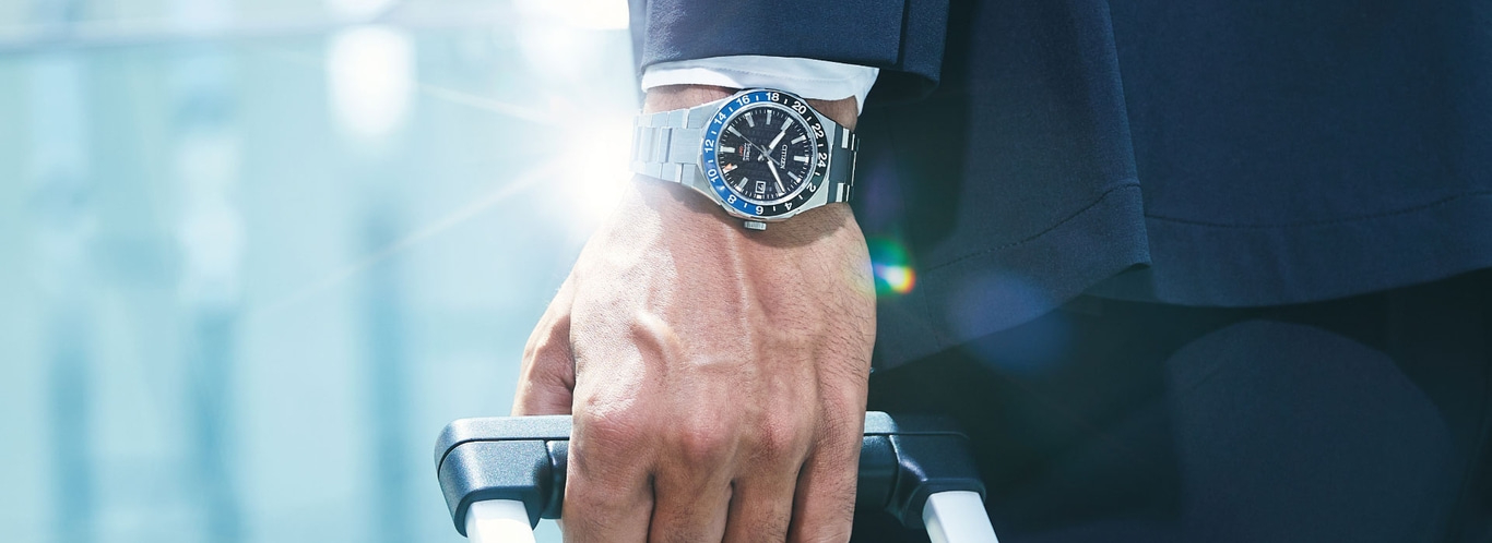 Mann mit Uhr, hält Koffer, stilvolles Reisen, Geschäftsreise, elegantes Outfit.