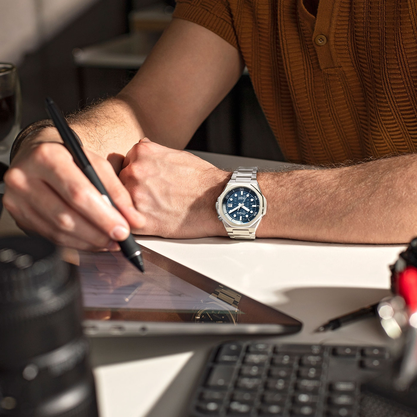 Mann arbeitet mit Tablet, Uhr am Handgelenk, Stift in der Hand.
