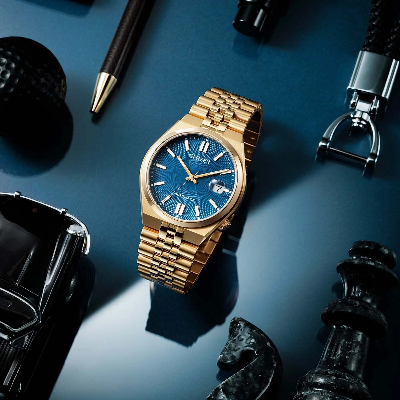 Montre dorée Citizen sur fond bleu avec des accessoires de loisirs.